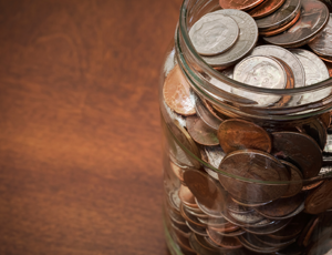 A jar full of coins on a wooden table.