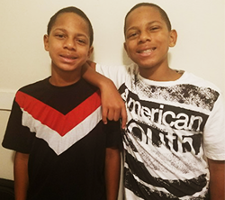 Two boys posing for a picture in front of a white wall.