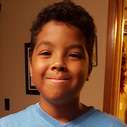 A young boy in a blue shirt is smiling.