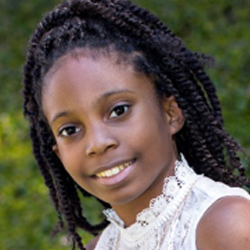 A young girl with dreadlocks smiling for the camera.