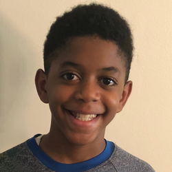 A young boy smiling in front of a wall.