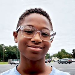 A young boy wearing glasses in a parking lot.
