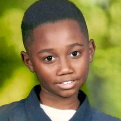 A young boy in a blue shirt is smiling for the camera.