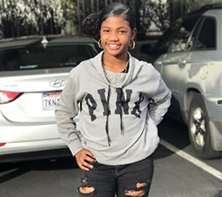 A young girl in ripped jeans and a hoodie standing in a parking lot.