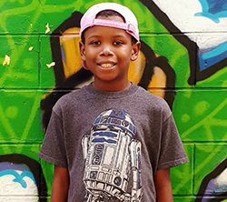 A young boy in a t - shirt standing in front of a graffiti wall.
