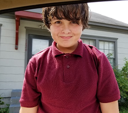 A young boy in a maroon shirt standing in a car.