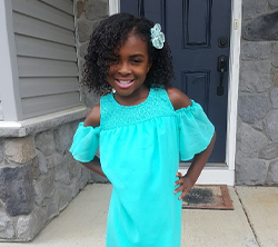 A young girl in a turquoise dress standing in front of a door.