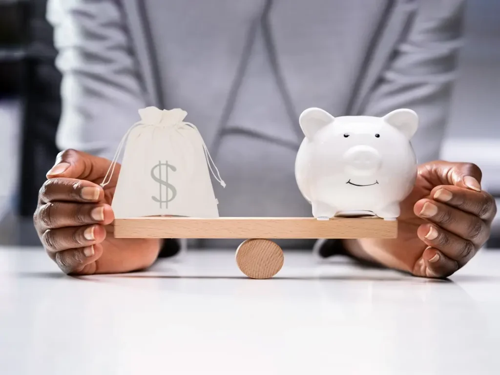 A woman holding a piggy bank and money bag on a seesaw.