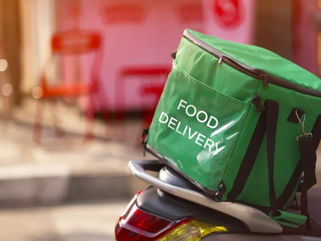 A green food delivery bag on the back of a motorcycle.
