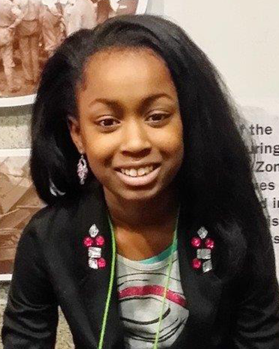 A young girl in a black jacket smiles at the camera.