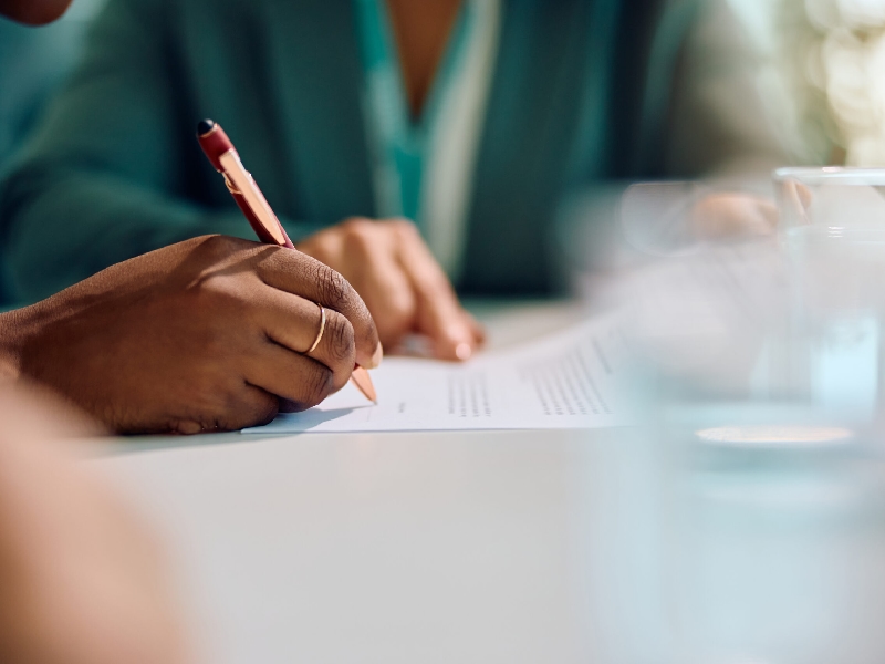 Close up of African American woman signing a contract with bank manager in the office.