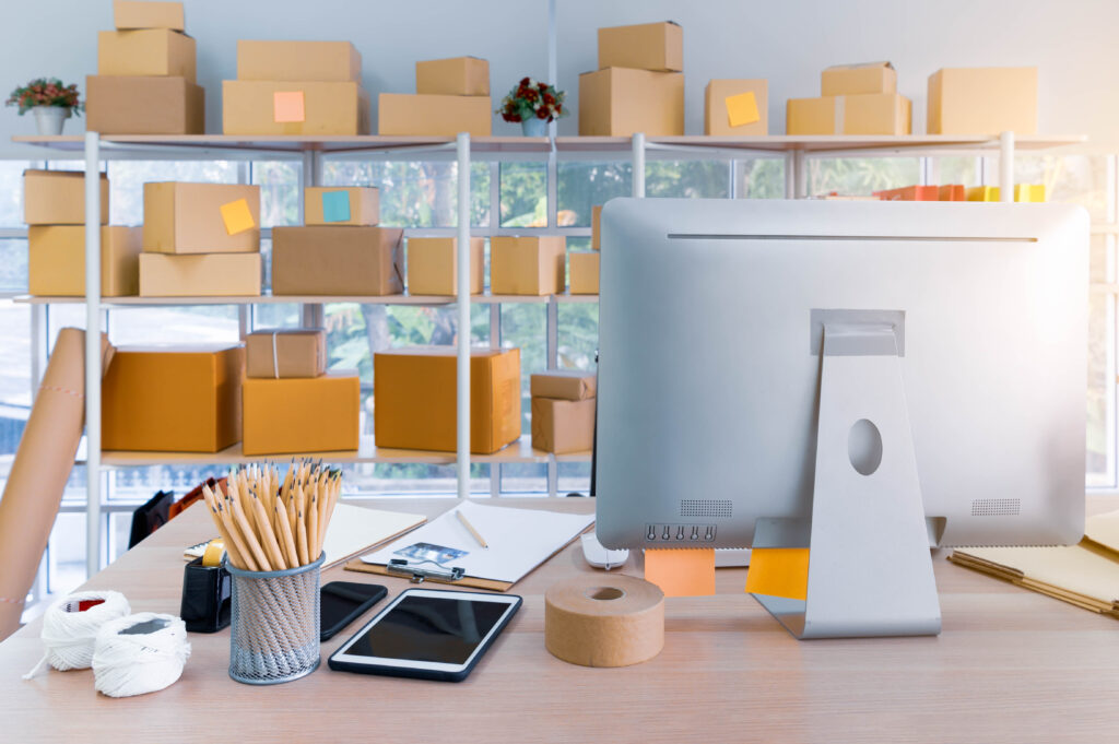 A workspace with a computer and shelves full of boxes in the background.