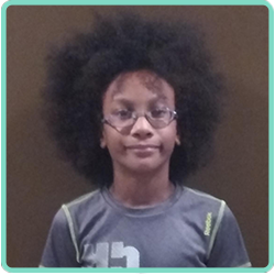 A boy with an afro and glasses is standing in front of a wall.