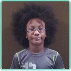 A boy with an afro and glasses is standing in front of a wall.