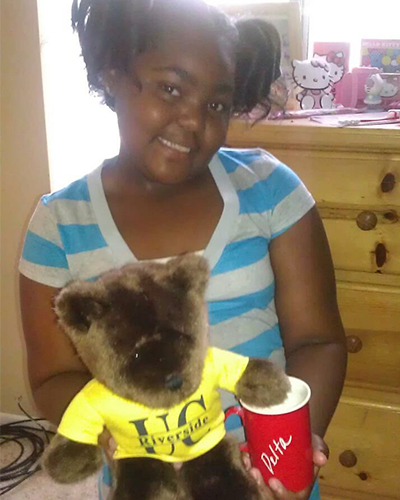 A girl holding a teddy bear and a cup.