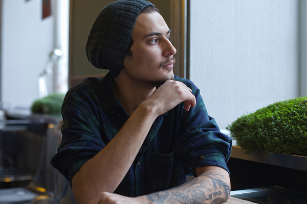 man wearing a hat sitting at a table and looking out a window