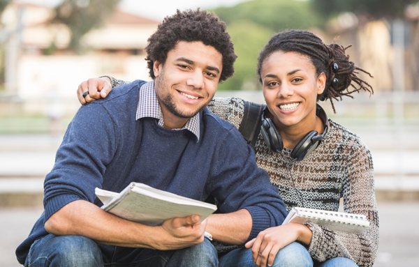 A young couple sitting on the ground with books in their hands.