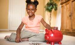 A little girl sitting on the floor with a piggy bank.