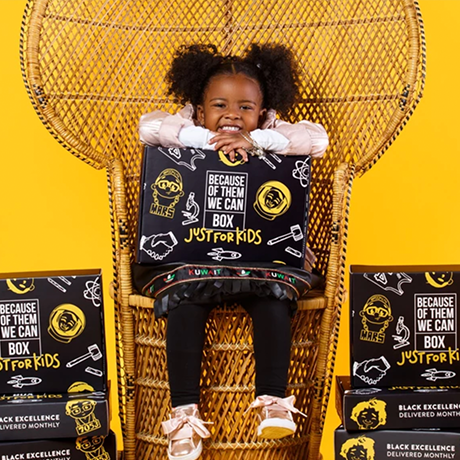 A little girl sitting in a wicker chair holding a box.