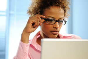 A woman wearing glasses is looking at her laptop.