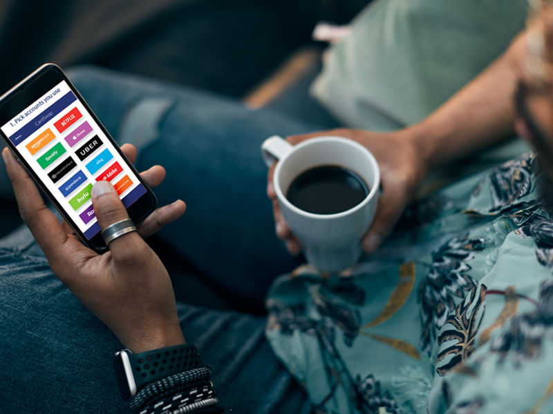 A person sitting on a couch with a smartphone and a cup of coffee.