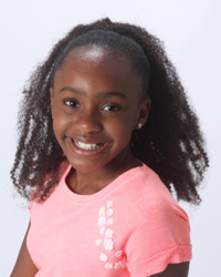 A young girl in a pink shirt smiles for the camera.