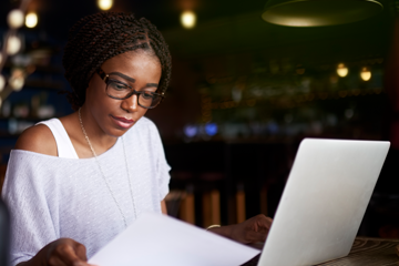 woman looking at a piece of paper next to computer