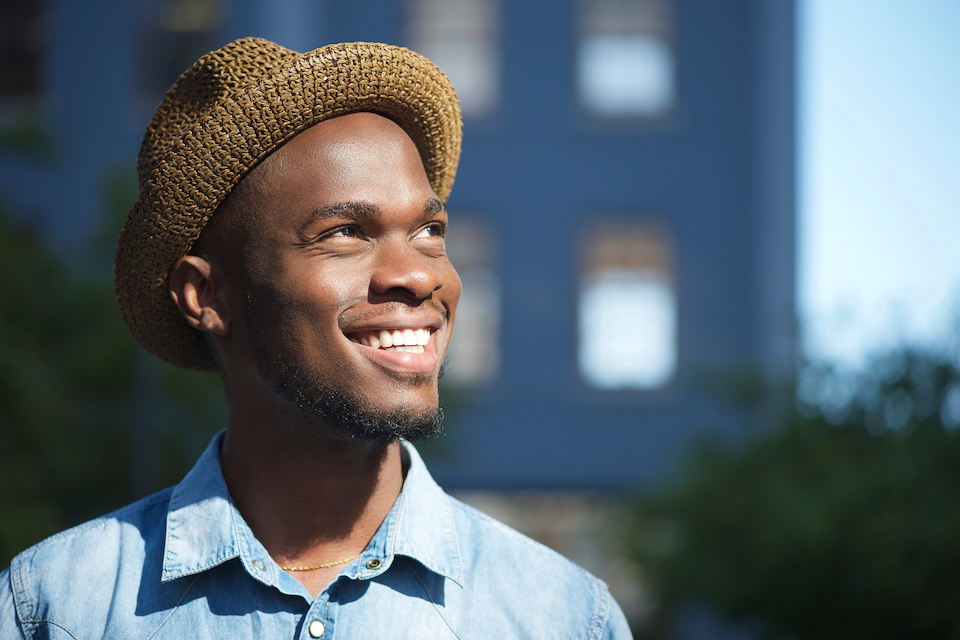 man wearing a hat standing outside and looking up toward the sun