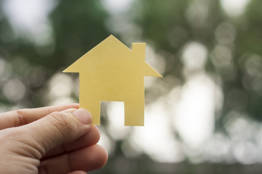 A person holding a paper house in front of a blurry background.