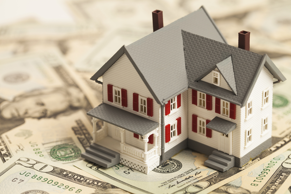 A house model on top of a pile of money.