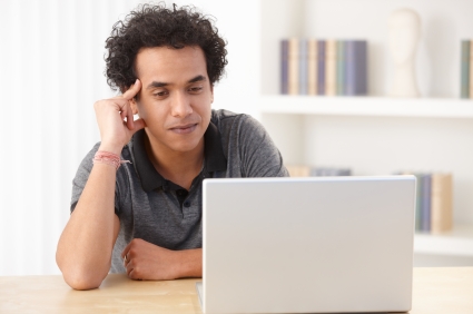 A young man sitting at a table looking at his laptop.