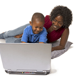 A woman and a boy laying on the floor with a laptop.