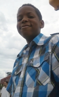 A young boy in a blue shirt is smiling in front of a truck.