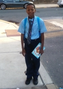 A boy in a blue shirt and tie standing on the sidewalk.