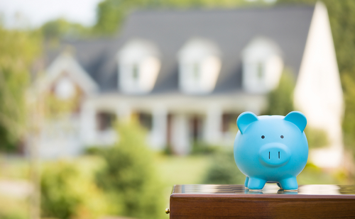 A blue piggy bank sitting on top of a table in front of a house.
