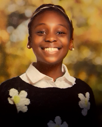 A young girl smiling in front of a tree.