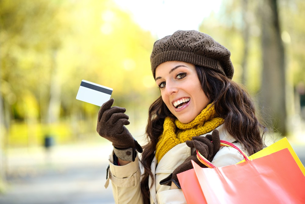 A woman holding a credit card and shopping bags.