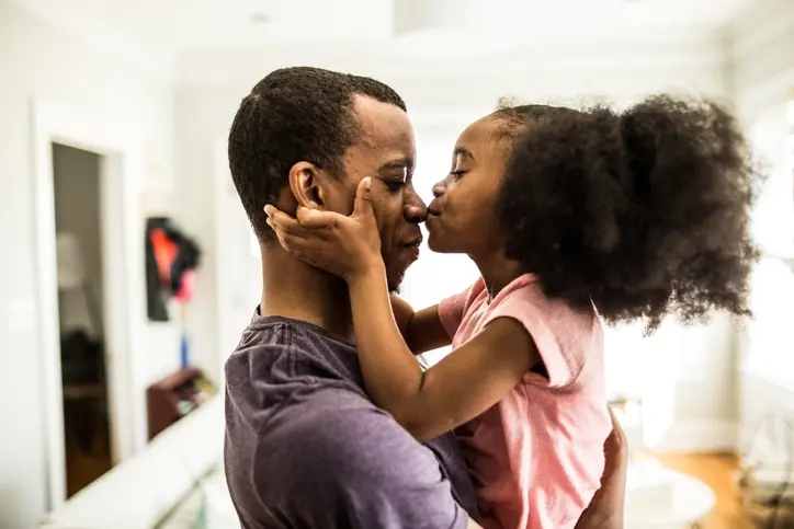 A man kisses his daughter in the living room.