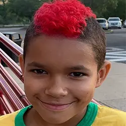 A boy with a red mohawk smiles for the camera.