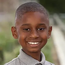 A boy in a gray shirt is smiling for the camera.