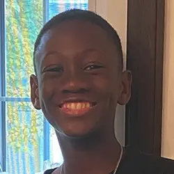 A young boy smiling in front of a window.