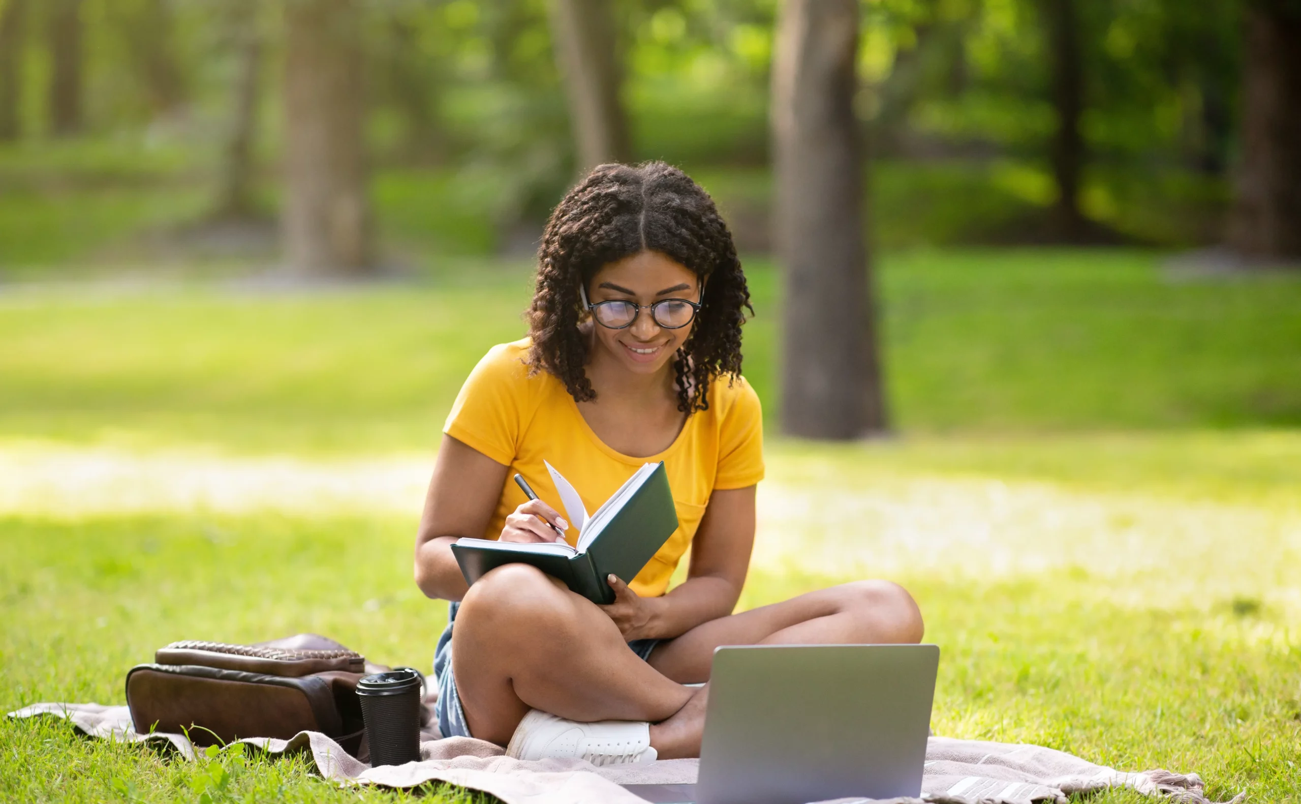 A young woman sitting on the grass with a laptop in her lap.