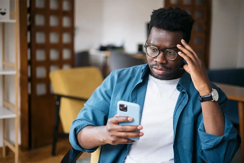 A black man looking at his phone while sitting in a chair.