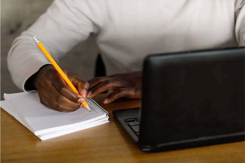 A man writing on a notebook with a pencil.