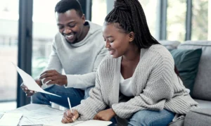 A man and woman sitting on a couch looking at paperwork.