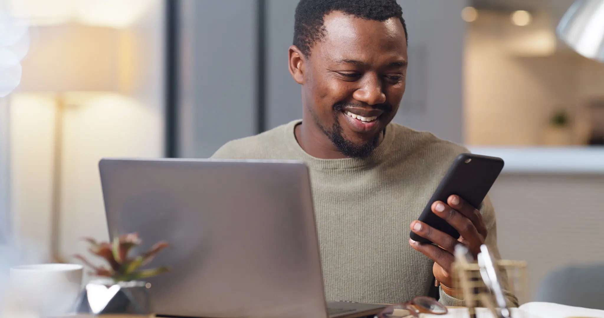 A black man is smiling while using a laptop.