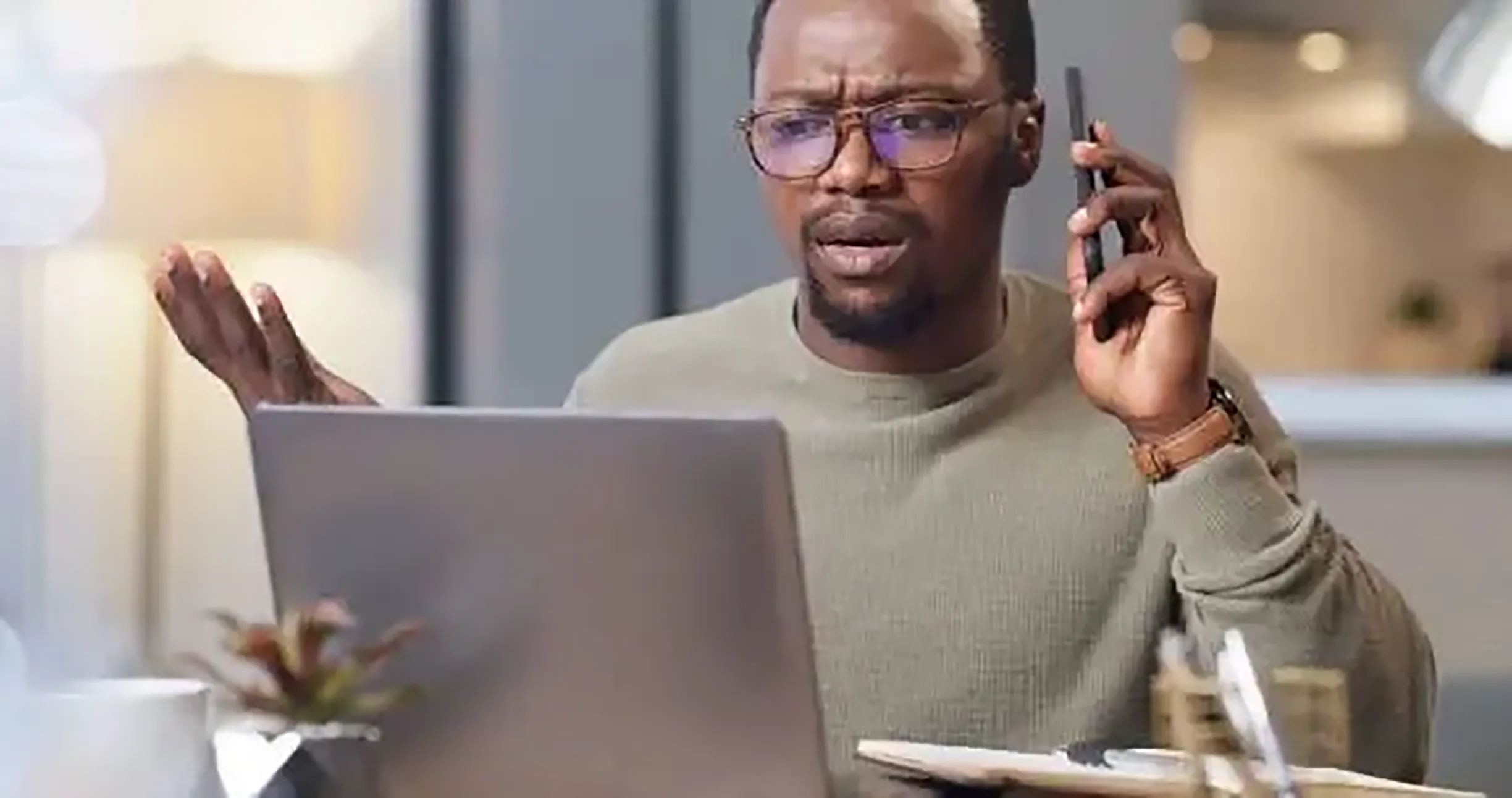 A man is talking on his phone while sitting at his desk.