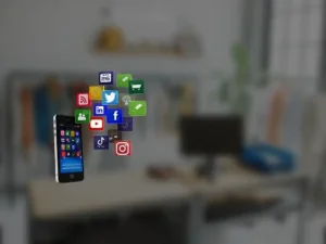A mobile phone with social icons flying in front of a desk.