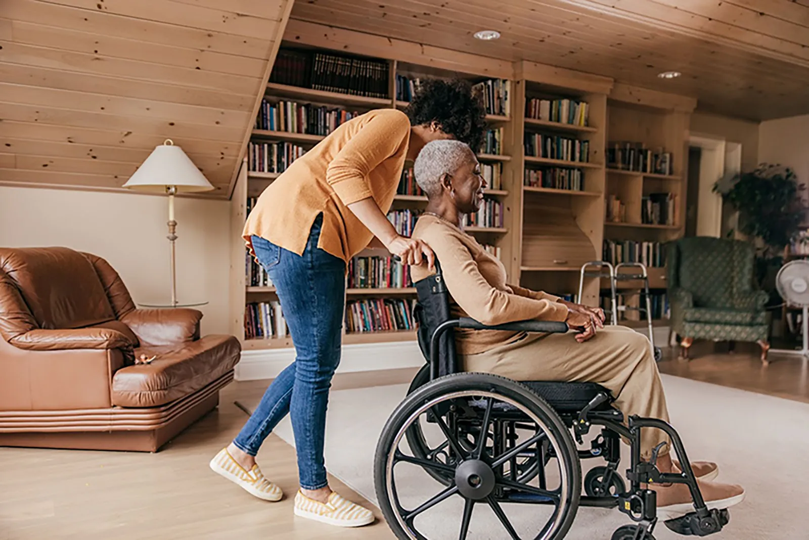 A woman helping an elderly man in a wheelchair in a living room.