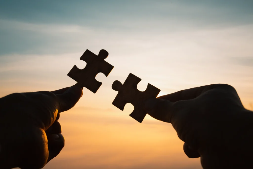 Two hands holding a puzzle piece as part of their financial planning at sunset.